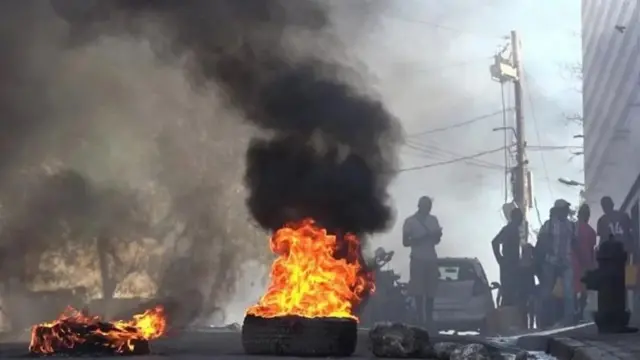 Varios hombres detrás de unos neumáticos en llamas en Puerto Príncipe. 