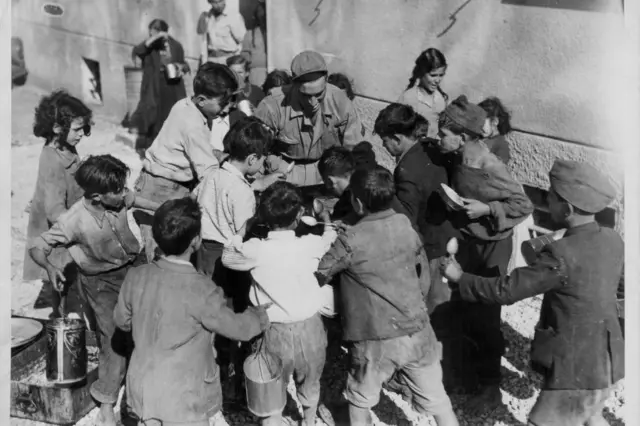 Niños se reúnen alrededor de una olla de comida.