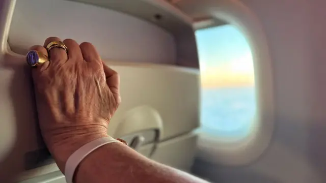 una mano aferrándose a un asiento de avión y en el fondo se ve el horizonte por la ventanilla 