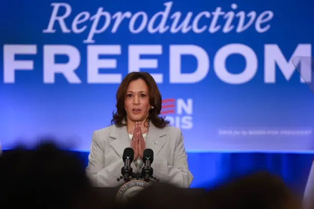 Kamala Harris con un cartel detrás que dice 