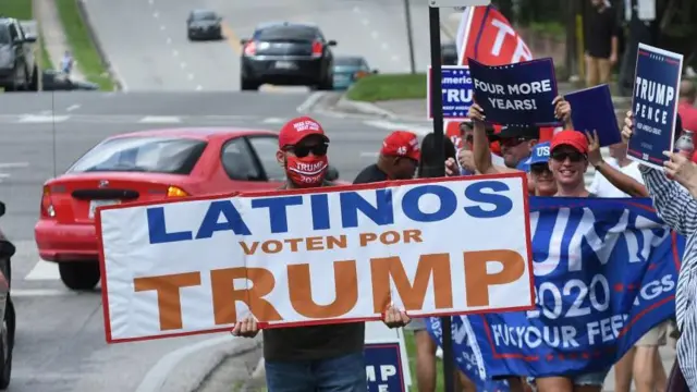 Personas que llevan gorras de Hagamos a Estados Unidos Grande Otra Vez sostienen carteles que dicen LATINOS VOTEN POR TRUMP