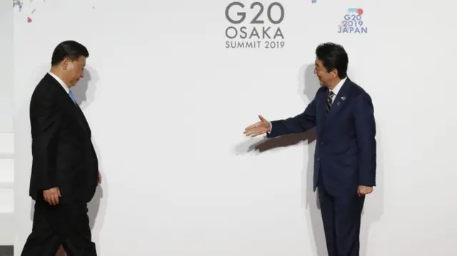 El presidente chino, Xi Jinping, baja la mirada mientras camina hacia el primer ministro japonés, Shinzo Abe, que le tiende la mano con una sonrisa.