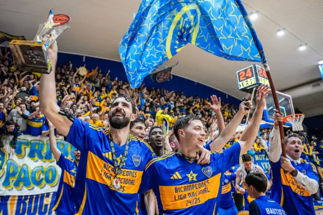 Sebastián Vega festeja el campeonato con la copa en su mano derecha, mientras abraza a uno de sus compañeros de equipo con el brazo izquierdo.