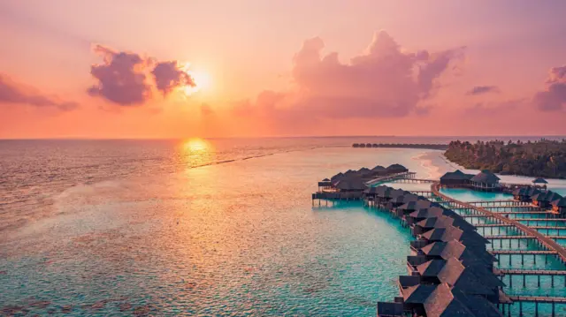 Atardecer en las Maldivas. Horizonte con nubes de colores sobre el mar y el muelle de la villa acuática.