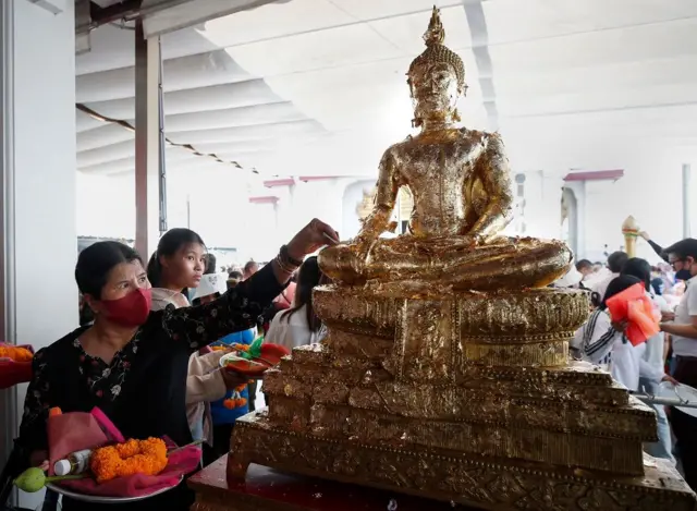 Una mujer coloca una ofrenda en un estatua de Buda