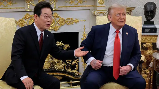 Lee Jae Myung y Trump están sentados uno al lado del otro en sillones amarillos en el Despacho Oval. Llevan trajes de colores oscuros con corbatas rojas. 