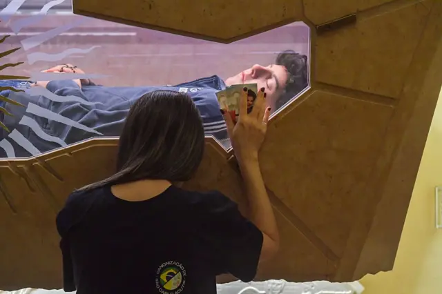 Una joven junto a la urna que tiene el cuerpo de Acutis