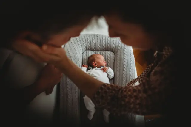 Bebé en la cuna y padres dándose una caricia.