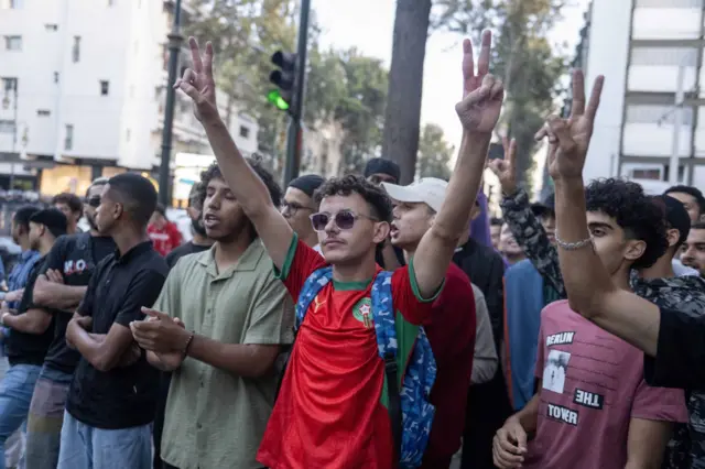 Jóvenes protestan en Rabat, Marruecos. En el centro de la imagen destaca un muchacho con camiseta roja, gafas de sol y los brazos en alto.