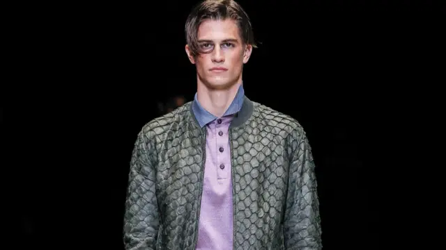 Primer plano de un modelo masculino que lleva una chaqueta de cuero gris pirarucu sobre un polo morado con cuello azul.