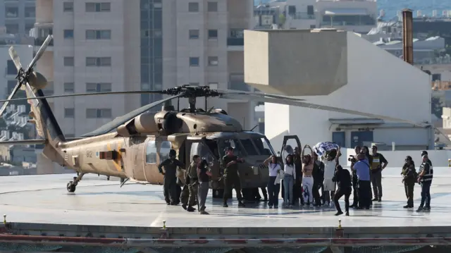 Un helicóptero militar en el techo de un edificio. Al lado hay un grupo de militares y otro de civiles que se abrazan y alzan los brazos. Uno sujeta una bandera.