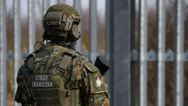 Un soldado armado de Polonia con rótulo en la espalda que lo identifica como un guardia fronterizo vigila una valla metálica