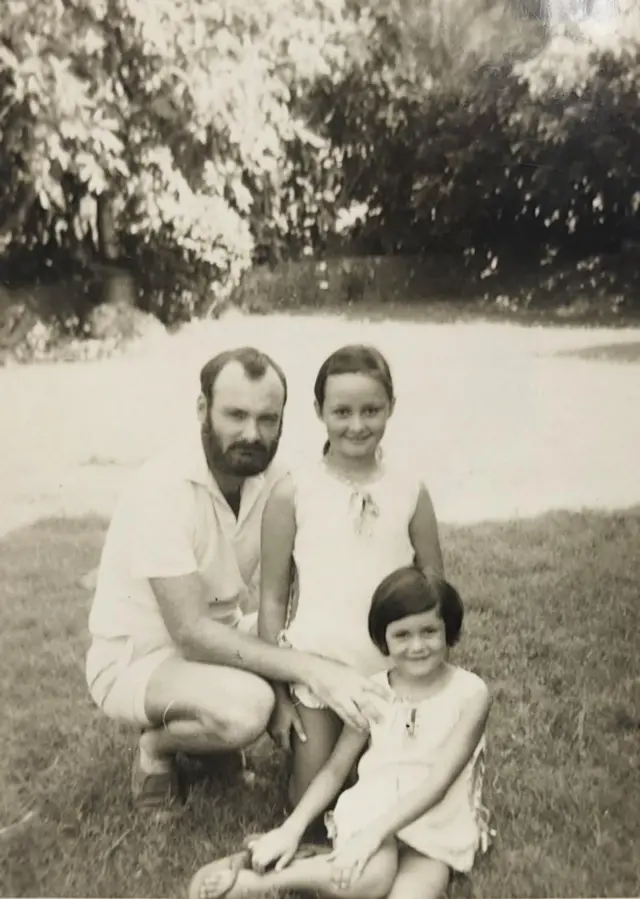 Michele, de diez años, aparece en el centro de una fotografía en blanco y negro de 1972 con su padre a la derecha y su hermana pequeña delante. Aparecen en un jardín soleado y llevan mangas cortas blancas o brillantes.