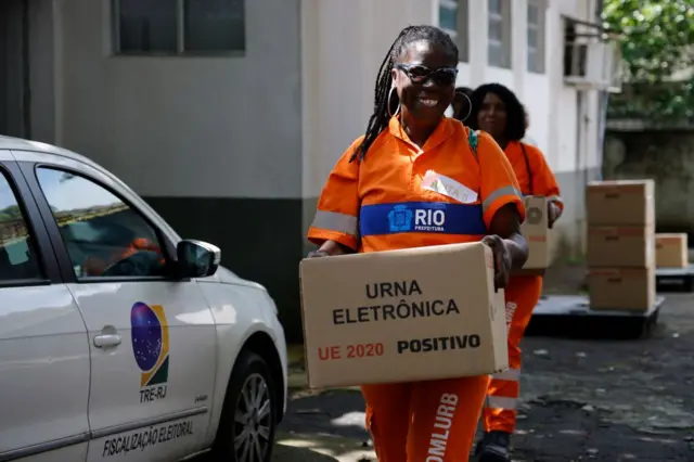Una mujer vestida con un uniforme de la alcaldía de Río de Janeiro sostiene una caja que dice 