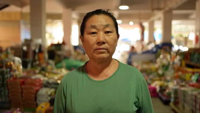 Li Mianzhen con una camiseta verde en el mercado donde arrienda un puesto