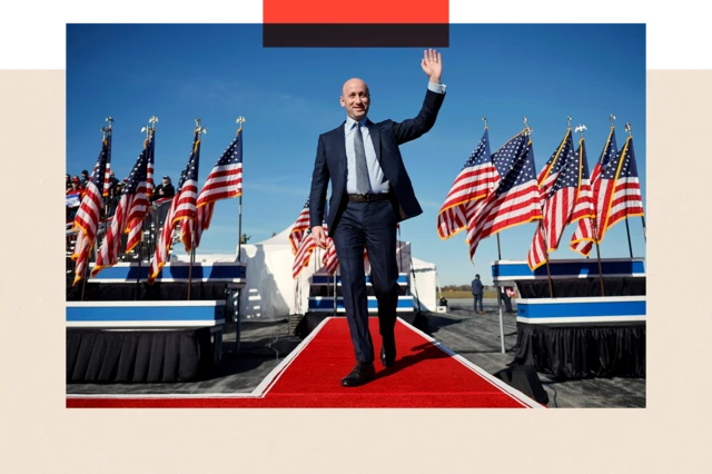 Stephen Miller llega a un mitin de campaña para el candidato presidencial republicano Donald Trump en el aeropuerto de Lancaster el 3 de noviembre de 2024 en Lititz, Pensilvania. Se lo ve caminando por una alfombra roja, con traje y saludando, con banderas estadounidenses a ambos lados.