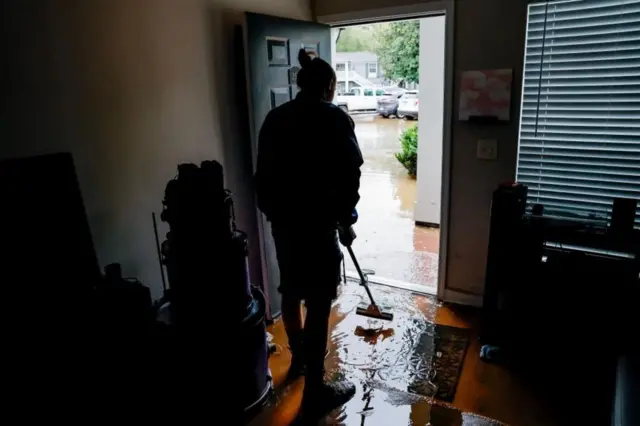 Un hombre escurre por la puerta principal el agua que inundó su casa. 