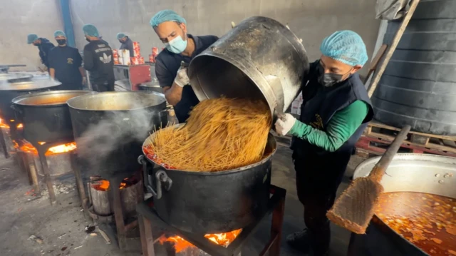 Varios cocineros preparan comida en una ollas gigantes.