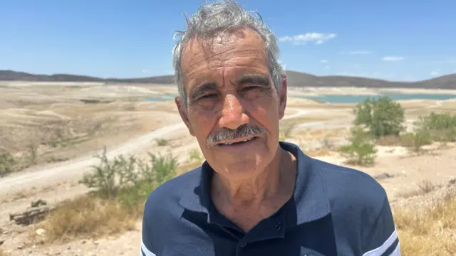 Trabajador voluntario Rafael Betance mira a cámara, parado frente a un panorama muy árido