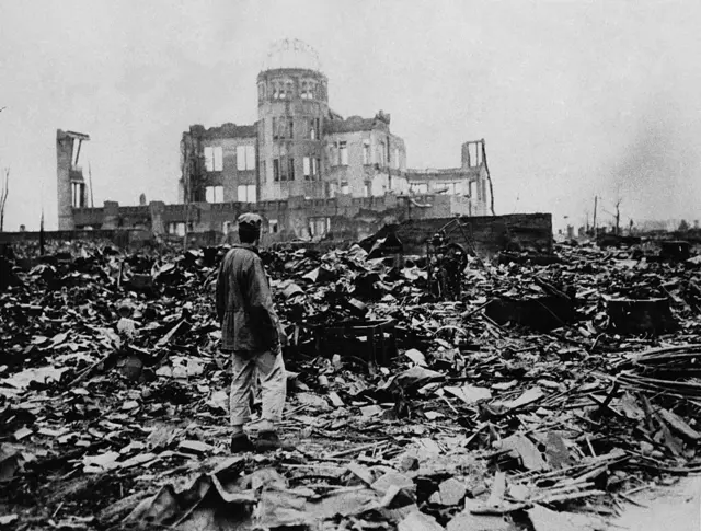 Un hombre se encuentra entre las ruinas de Hiroshima, con lo que queda de la estructura de un gran edificio frente a él, después de que una bomba atómica fuera lanzada allí.