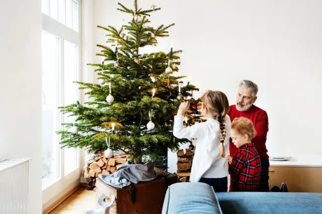 Un hombre y sus nietos decorando un árbol de Navidad.