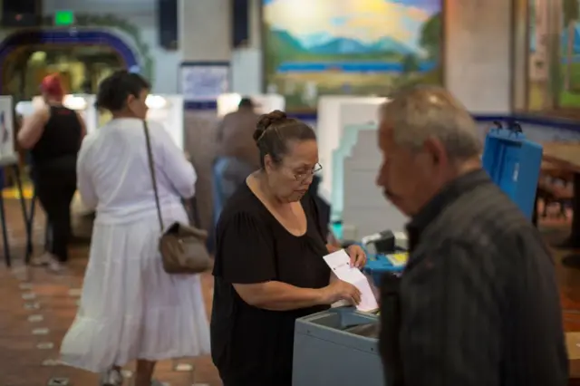 Una mujer sostiene una papeleta electoral en la estación de votación con otro hombre en primer plano