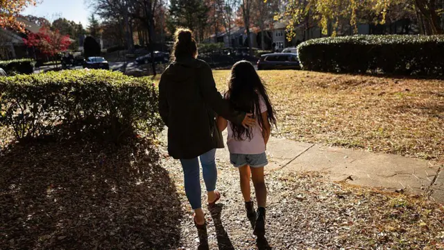 La inmigrante hondureña Sandra Sanchez acompaña a su hija Yanela, de 9 años, por el complejo de apartamentos el 17 de noviembre de 2025 en un lugar no especificado de Estados Unidos. Como muchos de sus compañeros estudiantes inmigrantes, Yanela se quedó en casa ese día debido a una operación de la Patrulla Fronteriza en la zona. Los padres temían que pudieran verse atrapados en la redada. La madre de Yanela, Sandra Sanchez, la llevó a Estados Unidos desde Honduras cuando tenía 2 años, cruzando el Río Bravo desde México hacia McAllen, Texas, el 12 de junio de 2018. Fueron detenidas durante varias semanas antes de ser liberadas para continuar con su proceso de asilo en la corte de inmigración de EE. UU. (Foto de John Moore/Getty Images)
