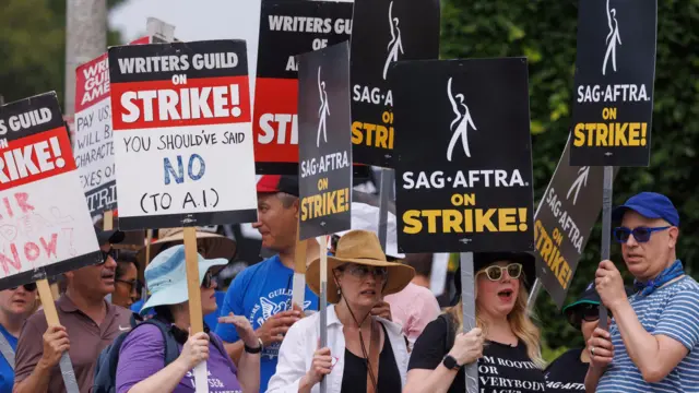 Miembros de los sindicatos de actores y guionistas de Hollywood marchan con carteles en Los Ángeles, California. Agitan pancartas que dicen 