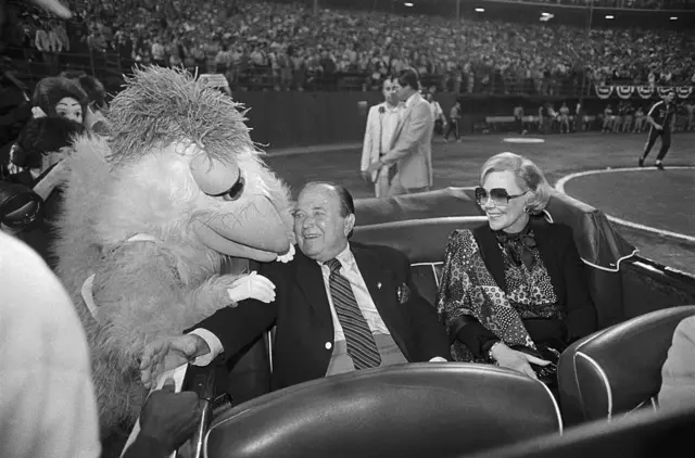 Joan con Ray Kroc en un auto con un personaje disfrazado de pollo