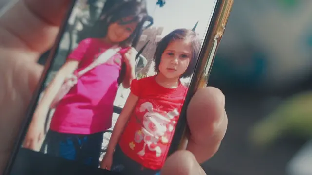 Dos niñas pequeñas con el pelo oscuro y camisetas rosas y rojas sonríen a la cámara en una foto que se muestra en un teléfono móvil.