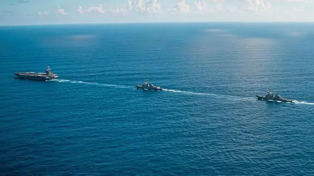 Un portaviones y dos barcos atraviesan un mar calmo.