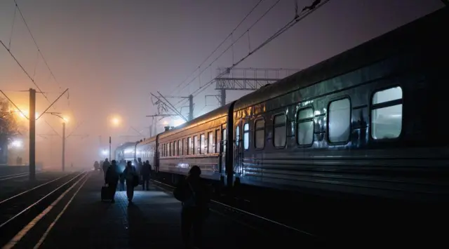 Personas caminan junto a un tren por un andén cubierto de niebla. 