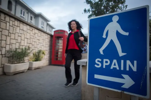 Mujer caminando al lado de una típica cabina de teléfonos británica de color rojo y, al otro lado y en primer plano, un cartel que indica que se puede ir caminando a