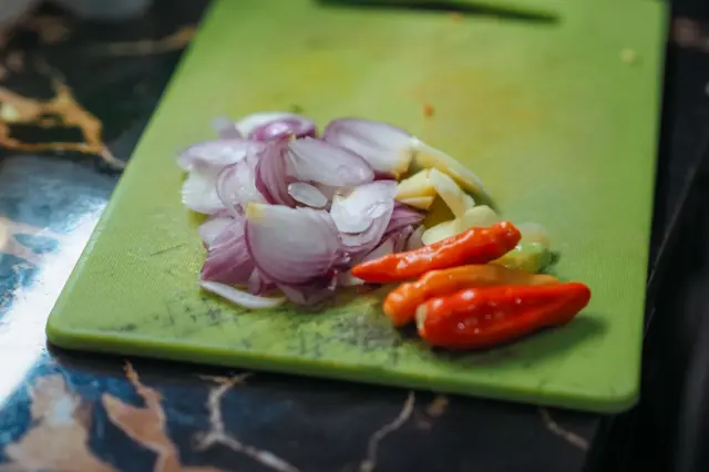 Jalapeños y cebollas en una tabla de picar verde de plástico.
