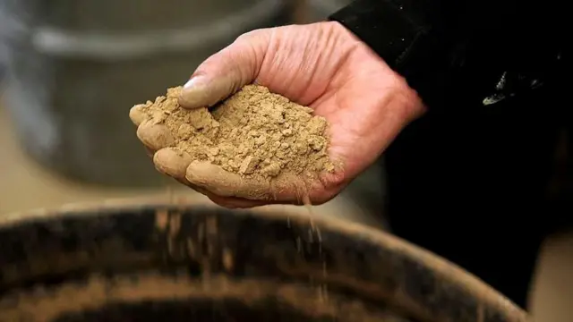 Una mano sostiene una sustancia arenosa de color café que contiene tierras raras