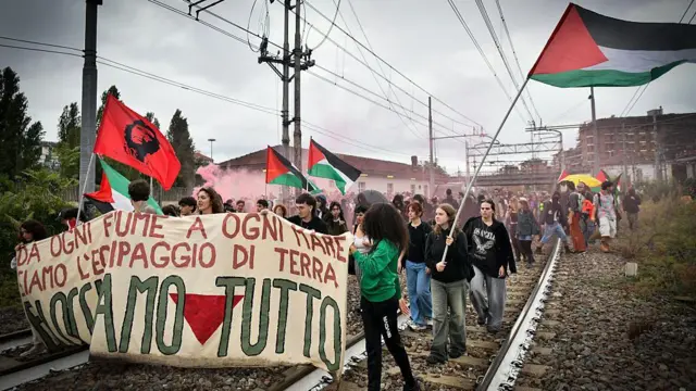 Manifestantes con banderas palestinas, una bandera con la imagen del Ché Guevara y una pancarta en italiano avanzan sobre las vías de un tren en Turín Italia.