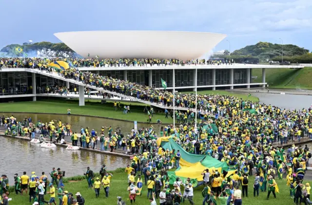 Una multitud de personas aglomeradas en torno a la Esplanada de los Ministerios en Brasilia. Algunos portan una bandera enorme de Brasil.