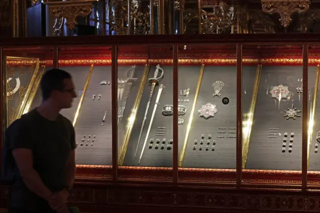 Una exhibición de una colección de artefactos históricos de intrincada elaboración del museo de la Bóveda Verde, que incluye espadas, joyas decorativas y otros objetos ornamentales.