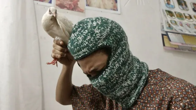 Un joven nigeriano encapuchado sostiene un paloma blanca que va a ser sacrificada.