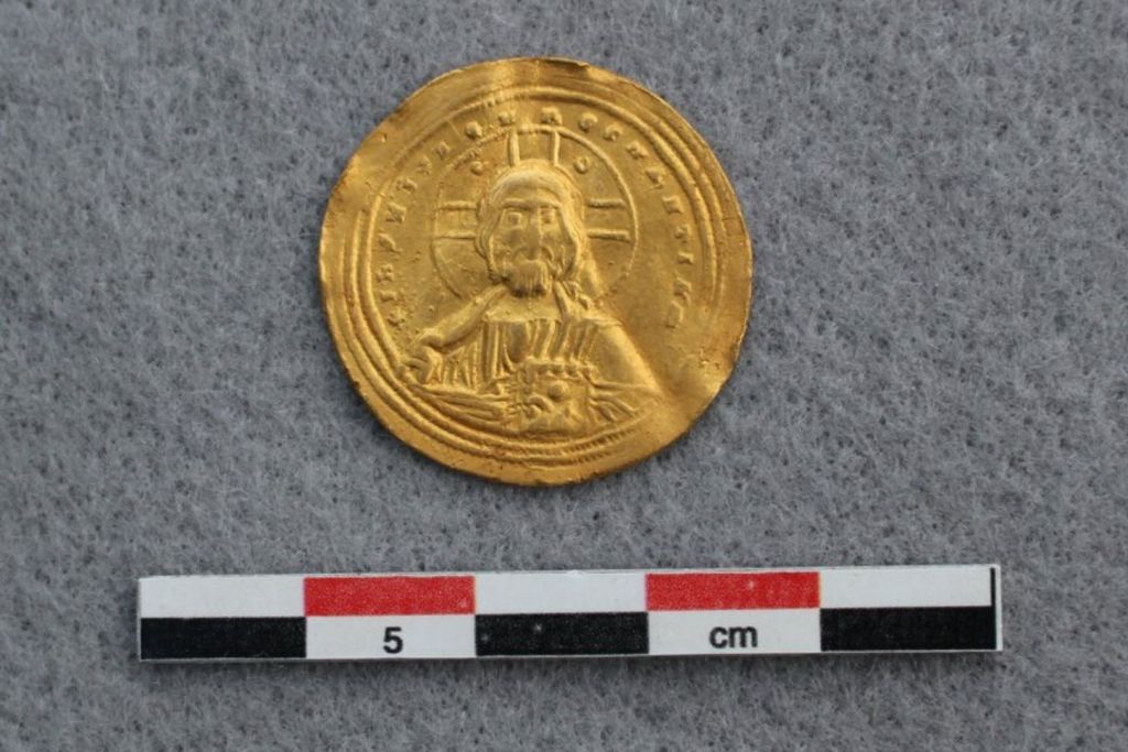En una de sus caras, la moneda muestra la figura de Cristo sosteniendo el libro sagrado, símbolo del poder espiritual en el Imperio Bizantino