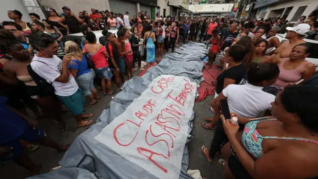 Personas se encuentran junto a los cuerpos de sus familiares asesinados por la policía junto a una pancarta que dice 