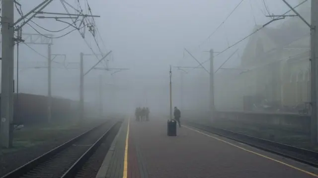Personas con uniforme militar en una estación de ferrocarril envuelta en la niebla. 
