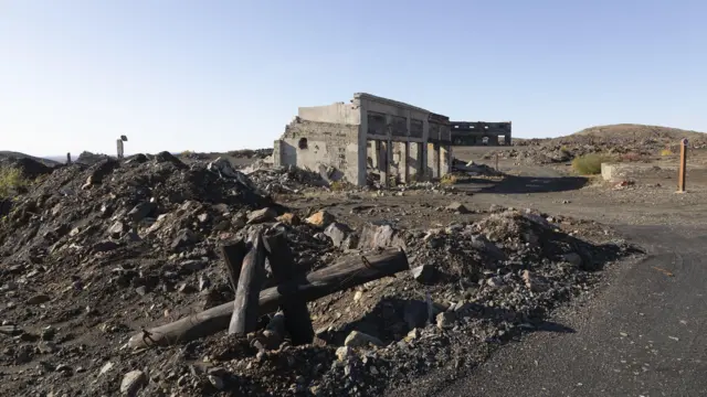 Un edificio en ruinas sobre un terreno pedregoso, bajo un cielo azul