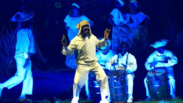 El artista puertorriqueño Bad Bunny sobre un escenario, con ropa blanca, y músicos detrás