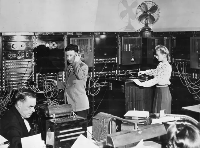 Vista de los operadores en la sala de control de Muzak, Nueva York, 1950. Supervisaban los programas de música de fondo y realizaban ajustes mediante un sistema similar a una central telefónica.