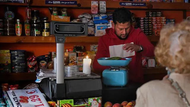 Un hombre vende en su tienda ilumindo por una vela en el mostrador.