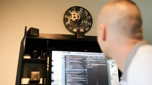 Un hombre mira una pantalla con el logo de bitcoin en lo alto. 