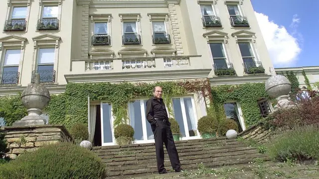 Un hombre vestido de negro se encuentra en los escalones frente a una casa.