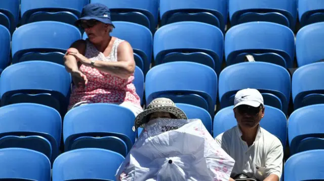 Una espectadora usa una sombrilla para protegerse del sol mientras otra se aplica protector solar durante el partido de tercera ronda de individuales masculino entre Gilles Muller de Luxemburgo y Pablo Carreño Busta de España en el quinto día del torneo de tenis Abierto de Australia en Melbourne el 19 de enero de 2018.