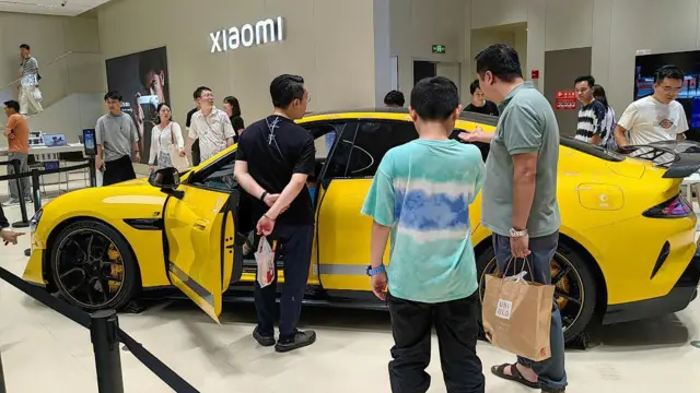 Un automóvil amarillo en un centro comercial está rodeado de personas. El el fondo, un letrero de Xiaomi